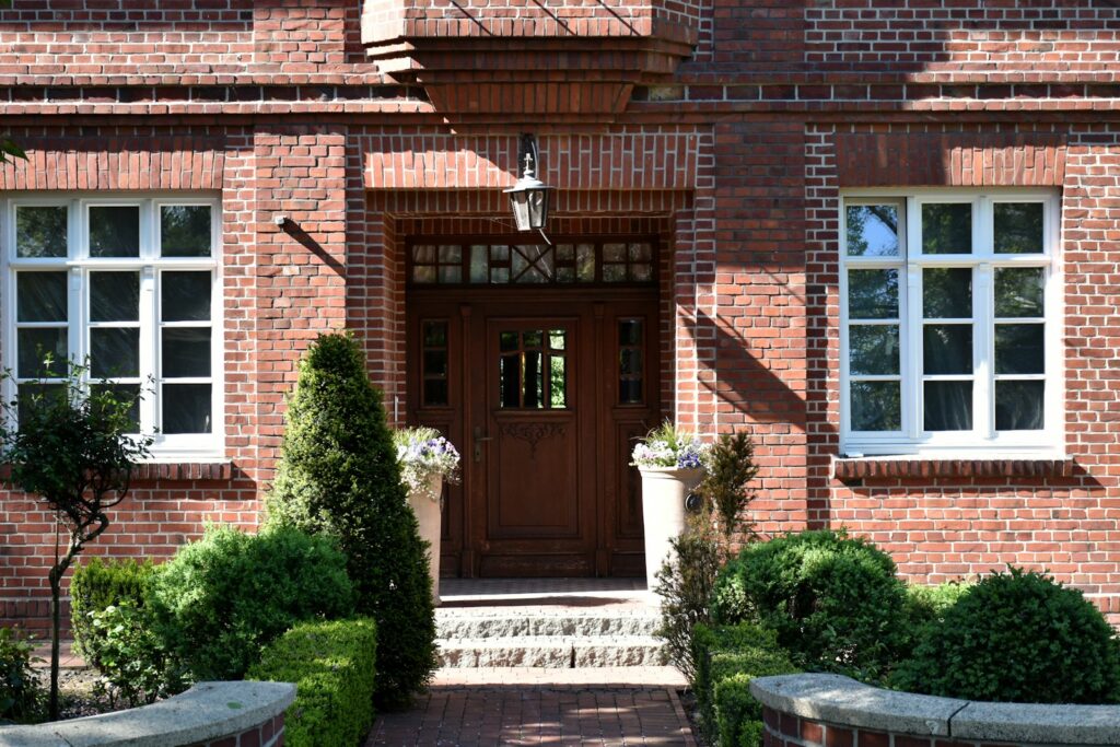 Eingang eines gepflegten Backsteinhauses mit weißen Sprossenfenstern